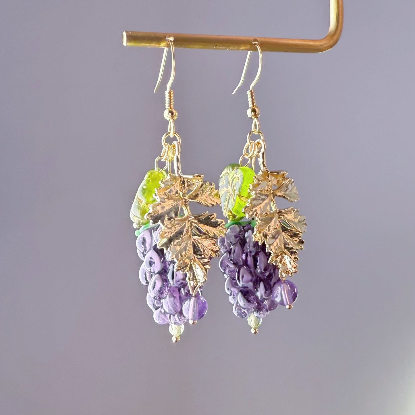 Gold leaf and purple bead earrings on a gray background