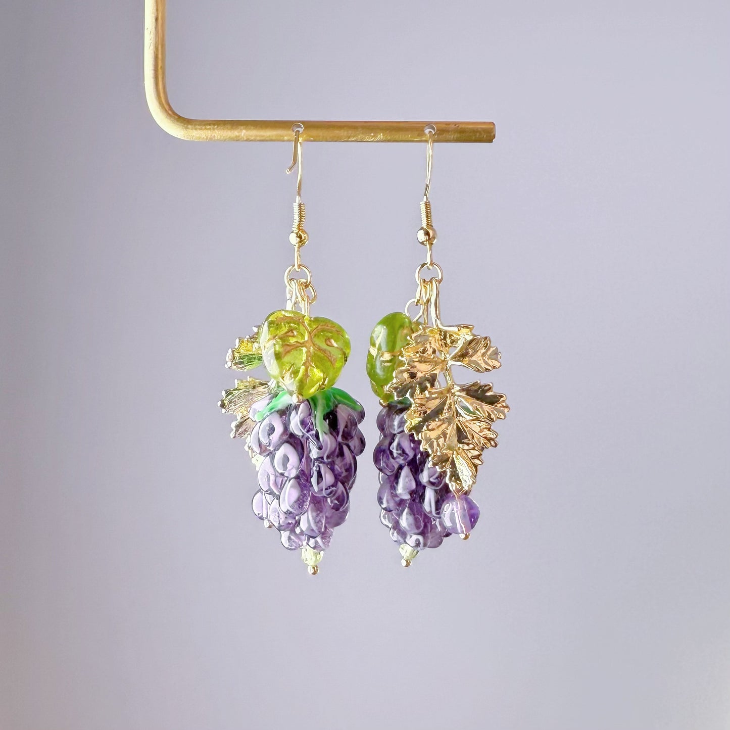 Grape-shaped earrings with gold leaves on a gray background
