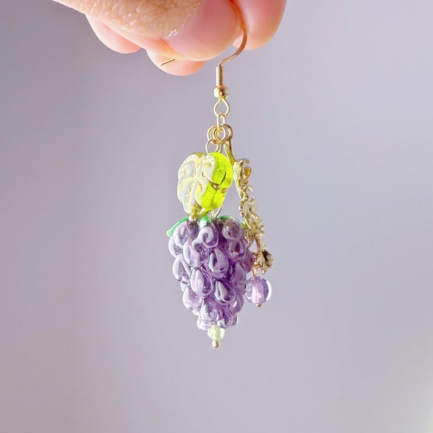 Earrings shaped like grapes held by a hand against a plain background