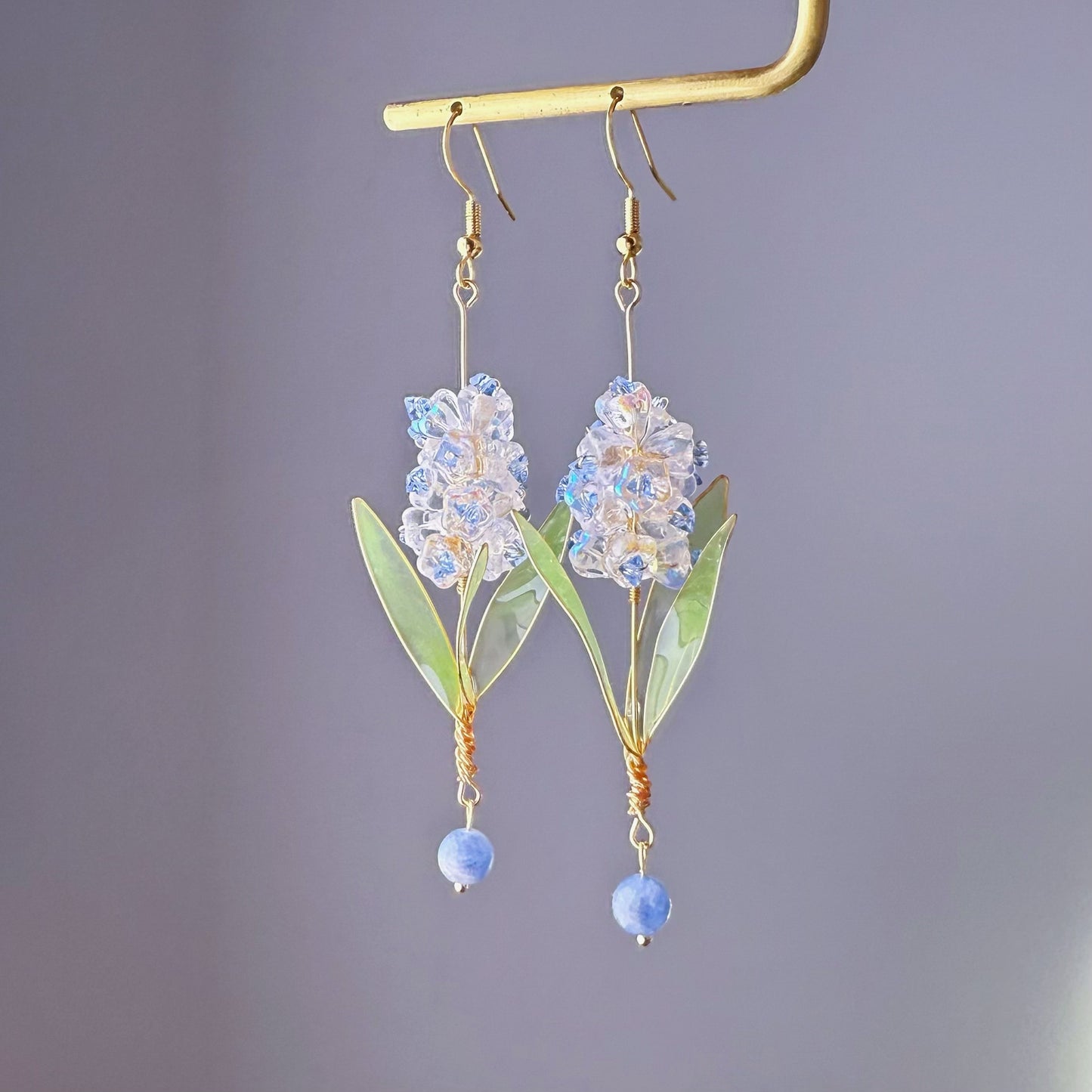 Decorative earrings with blue beads and green leaves on a gold stand against a gray background