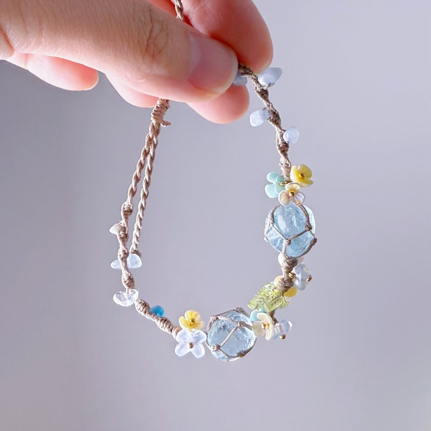 Hand holding a delicate bracelet with colorful beads against a neutral background