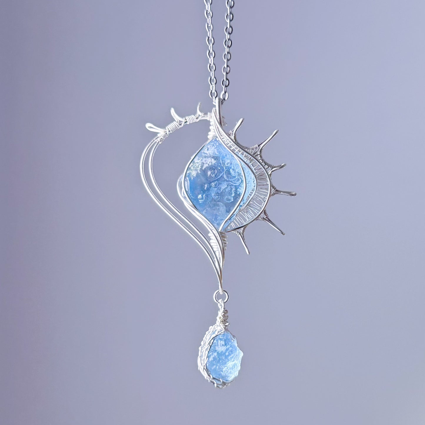 Silver pendant with blue gemstone on a light purple background