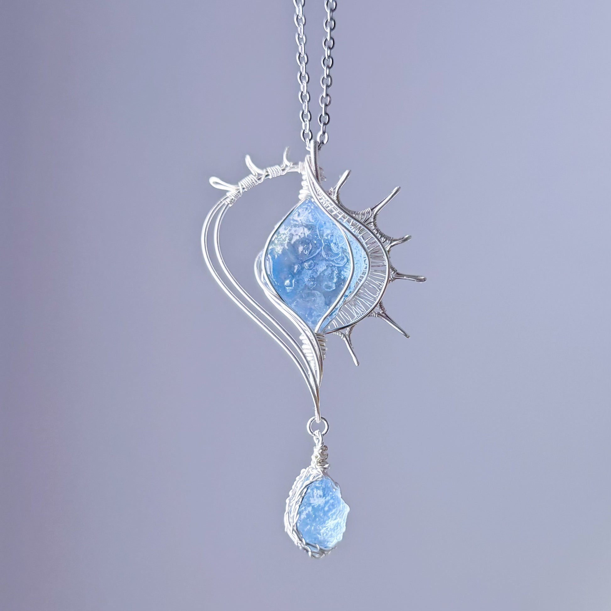 Silver pendant with blue gemstone on a light purple background