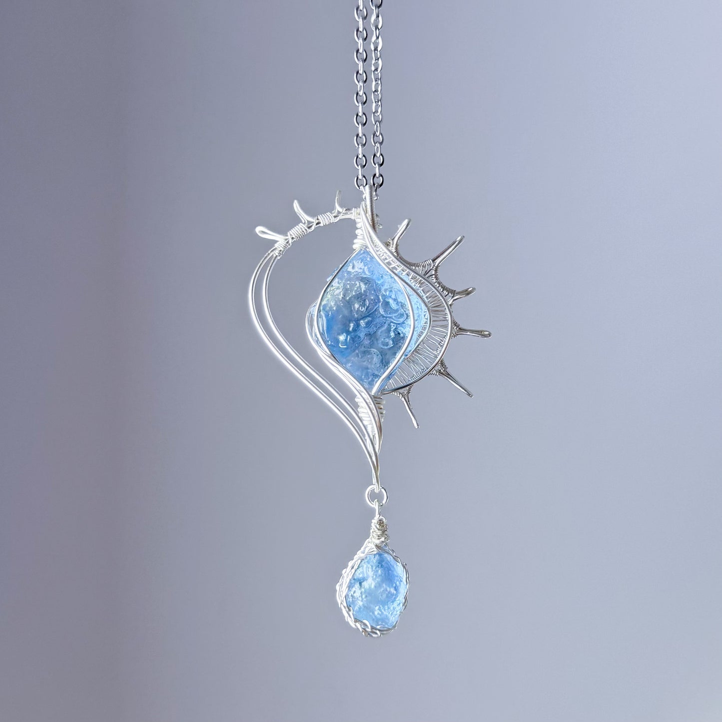 Silver necklace with a blue pendant on a gray background