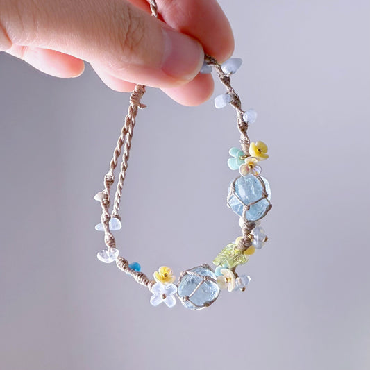 Hand holding a delicate bracelet with colorful beads against a neutral background
