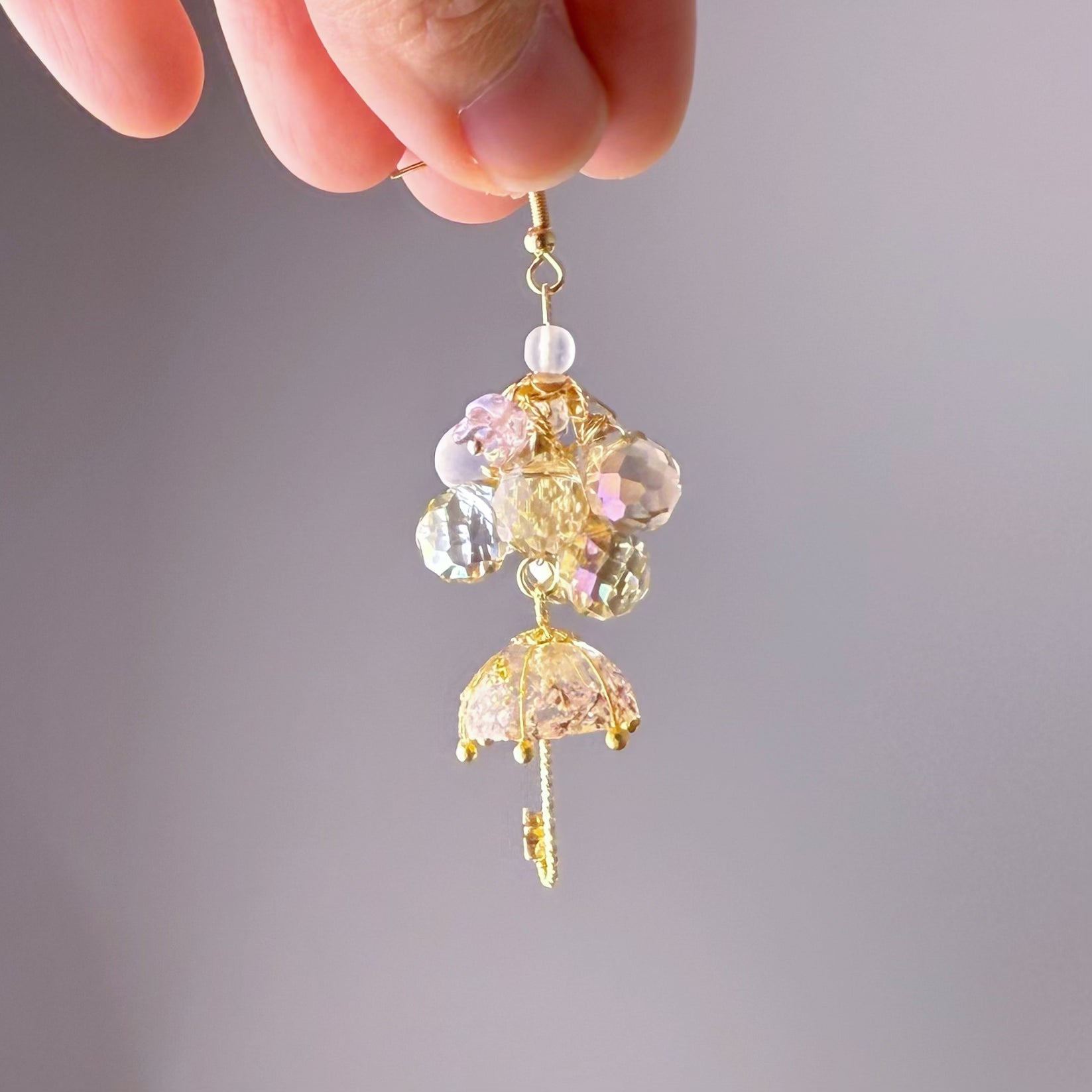 Delicate gold and crystal earring held by a hand against a gray background