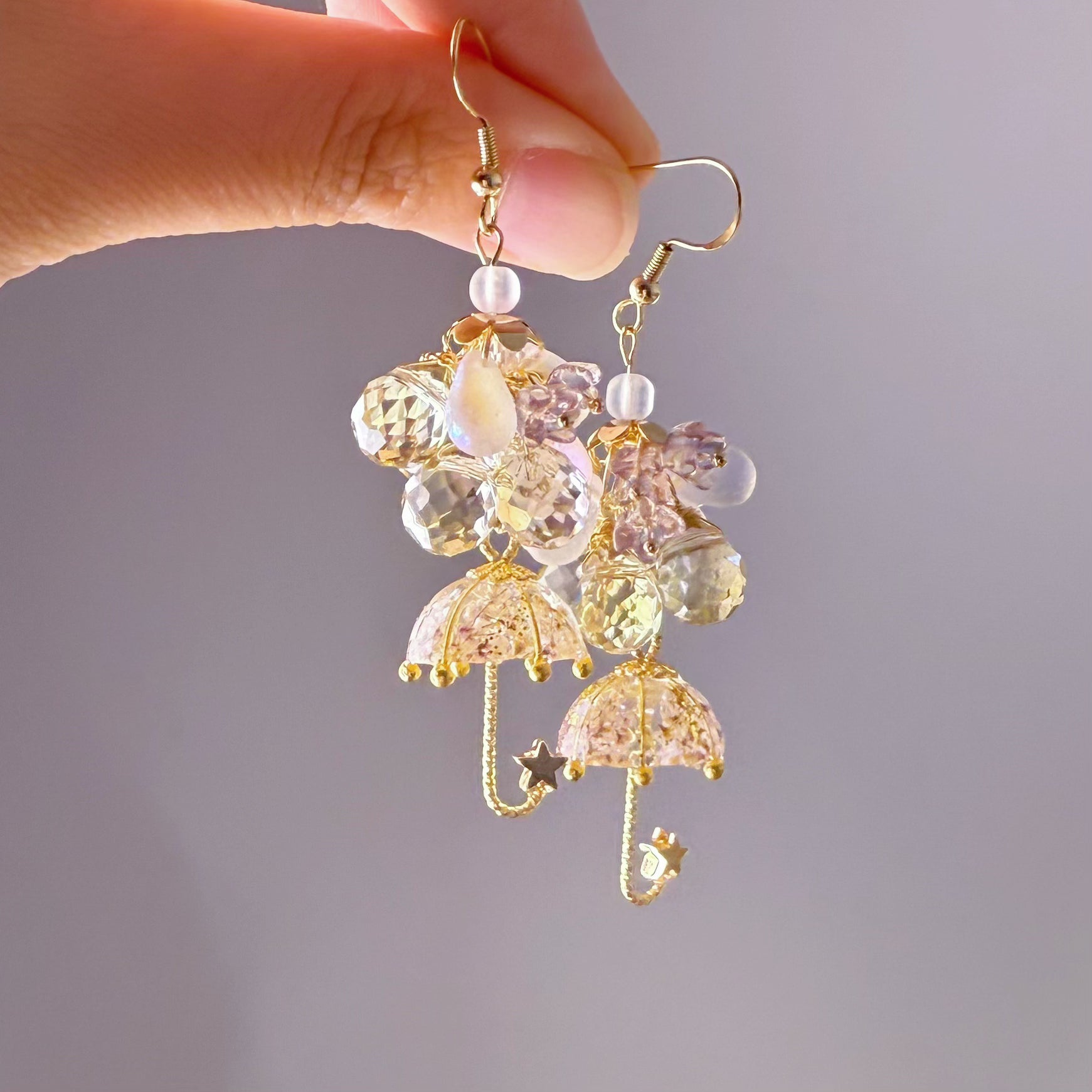 Decorative earrings with colorful beads and gold accents held by a hand against a neutral background