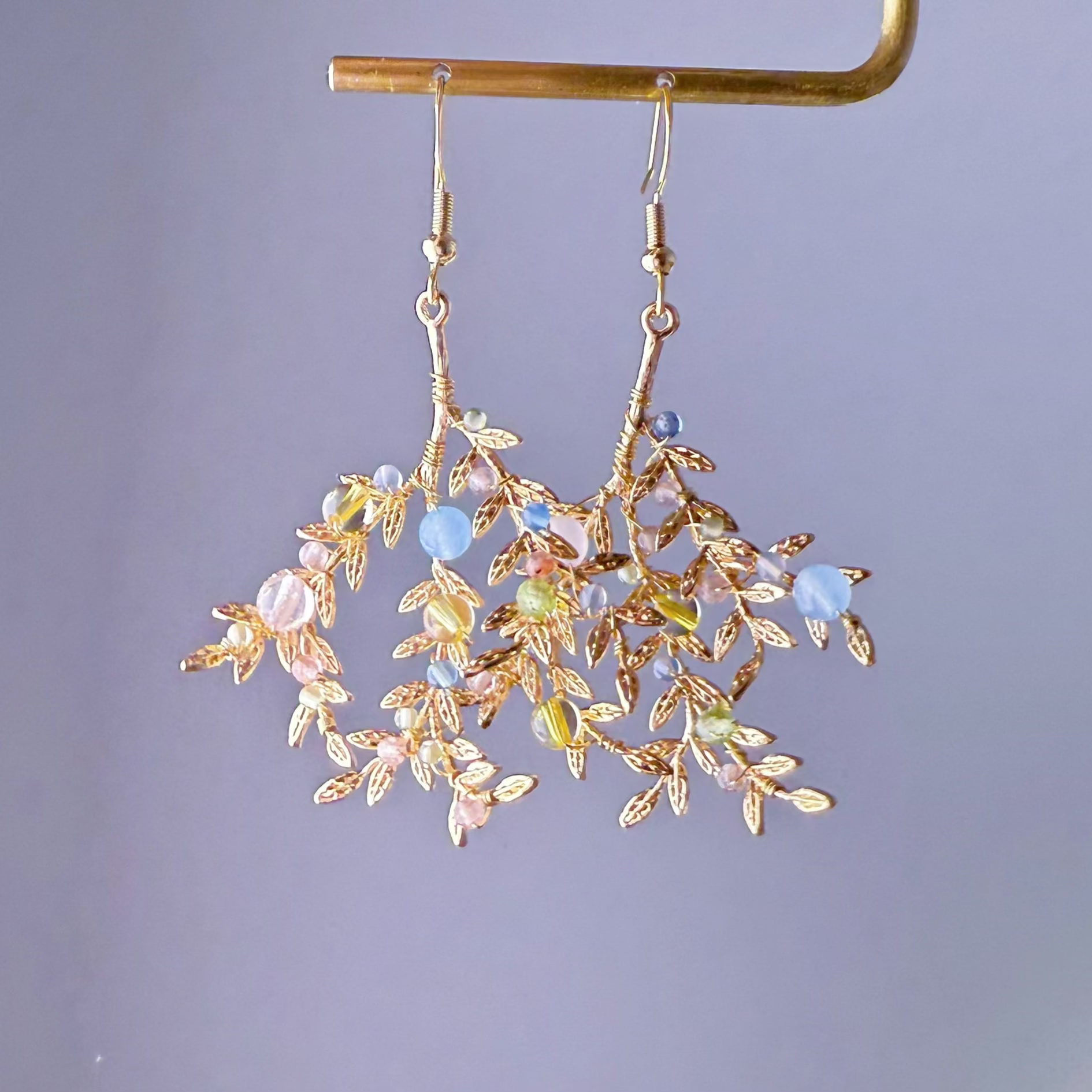 Gold leaf earrings with colorful beads on a gray background