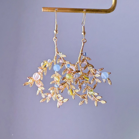 Gold leaf earrings with colorful beads on a gray background